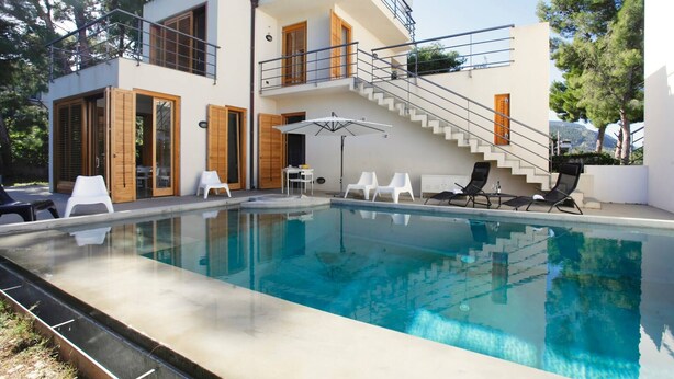 A modern two-story house with a swimming pool, outdoor seating, and a staircase leading to the upper floor.