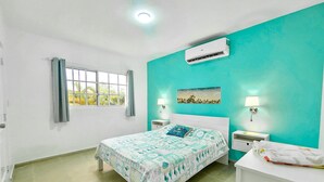 A bedroom with a bed, a window, an air conditioner, a nightstand, and a wall-mounted lamp. - Your Home 2 Miles to Private Access Beach (Punta Cana)