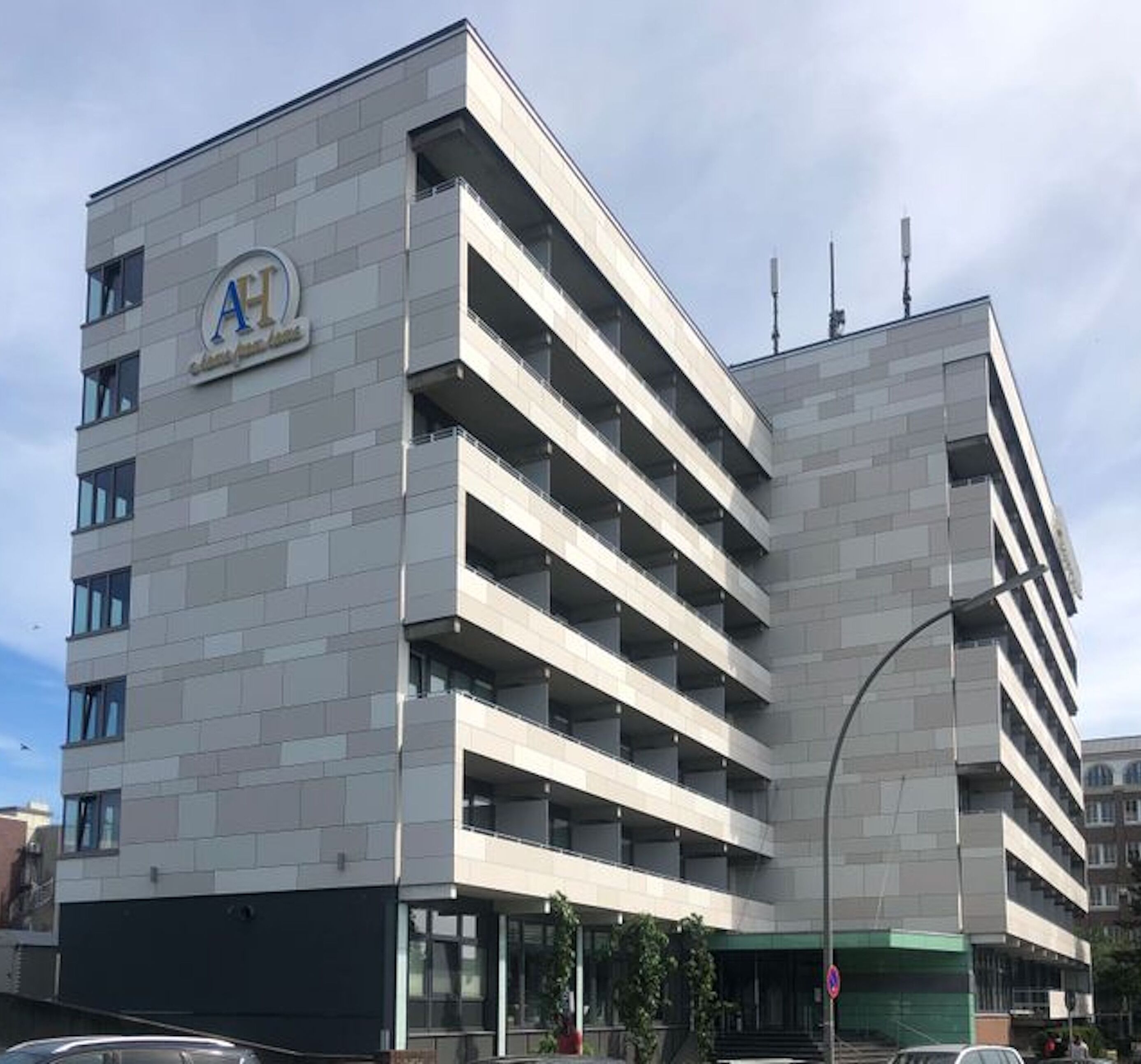 Ein mehrgeschossiges Gebäude mit einem auffälligen 'AH'-Logo, einer glatten Fassade und einer Tiefgarage.