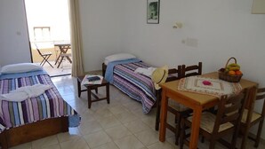 A room with two beds, a dining table with chairs, a small table with a basket of fruit, and a window with curtains. - Spacious Family Apartment With Sea View And Swimming Pool (Rethymno)
