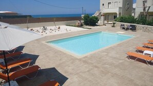 A swimming pool with lounge chairs, a view of the sea, and a building with a stone facade. - Spacious Family Apartment With Sea View And Swimming Pool (Rethymno)