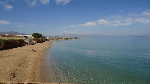 A beach with clear water, a wooden railing, and buildings in the background. - Spacious Family Apartment With Sea View And Swimming Pool (Rethymno)