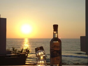 A bottle of Raki on a balcony with a sunset view over the ocean. - 3 Bedrooms Apartment With Sea View and Swimming Pool (Rethymno)