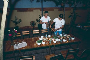 Une table de salle à manger en bois, dressée avec différents plats et boissons, entourée de chaises.
