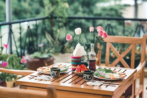 Una mesa de madera con platos de comida, una botella de bebida y un florero con flores.