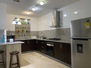 Eine moderne KĂŒche mit dunklen SchrĂ€nken, einem EdelstahlkĂŒhlschrank, einem Gasherd und einer Mikrowelle.