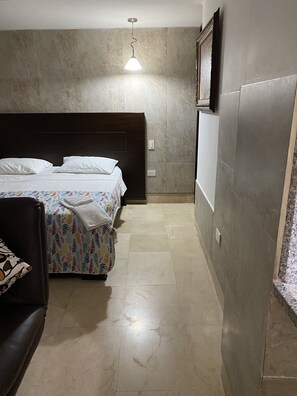 Ein Schlafzimmer mit einem Bett, einem Nachttisch, einem Sessel und einer Pendelleuchte.