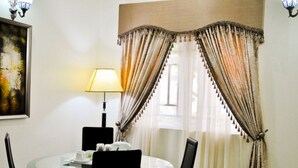 Ein Essbereich mit einem runden Glastisch, schwarzen Stühlen, einer Lampe und Vorhängen.