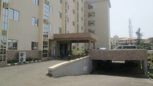 Un edificio de varios pisos con entrada central, unidades de aire acondicionado y un área de estacionamiento.