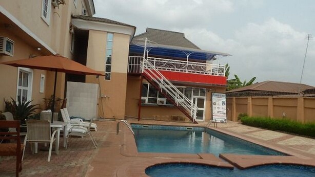 Una piscina con un deck rojo y blanco, un área techada con escaleras y sillas de descanso.