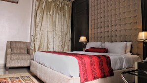 A bedroom with a bed, two bedside lamps, a chair, and a wall-mounted air conditioner. - Room-best Western Plus-guest Room (Ibadan)