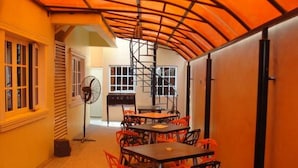 A room with tables and chairs, a fan, and a window with blinds. - Room-blueseasons Hotel & Suites- Guest R (Lagos)