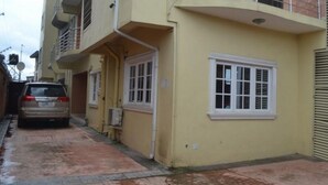 A yellow building with a garage door, a window, and a car parked outside. - Room-blueseasons Hotel & Suites- Guest R (Lagos)