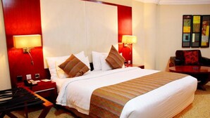 A hotel room with a large bed, two bedside tables, a desk, a chair, and two wall-mounted lamps. - Room-chelsea Hotel - Guest Room (Abuja)