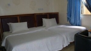 A double bed with a wooden headboard, a small black chair, and a window with blue curtains. - Room-definite Destiny Hotel - Guest Roo (Asaba)