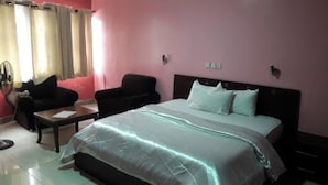 A hotel room with a bed, a sofa, a small table, and curtains. - Room-divine Fountain Hotel - Guest Room (Lagos)