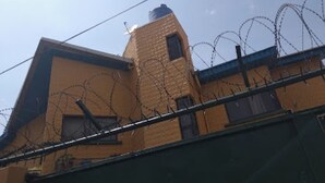 A building with a yellow facade, a small window, and barbed wire on the roof. - Room-divine Fountain Hotel - Guest Room (Lagos)