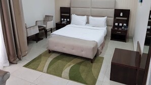 A hotel room with a bed, bedside tables, a chair, a desk, and a nightstand. - Full Moon Hotel - Premiere (Owerri)