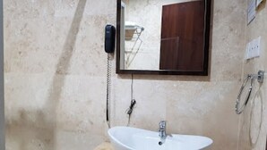 A bathroom with a white sink, a mirror, a telephone, and a shower area. - Full Moon Hotel - Premiere (Owerri)