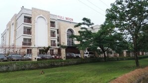A building with a sign reading 'FULL MOON' and a fenced parking area with cars. - Full Moon Hotel - Premiere (Owerri)
