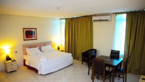 Ein Hotelzimmer mit Bett, Nachttisch, Lampe, Schreibtisch, Stühlen und Vorhängen.