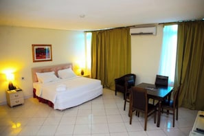 A hotel room with a bed, bedside table, lamp, desk, chairs, and curtains.