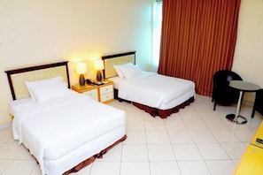 A hotel room with two beds, a nightstand with lamps, a small table, and a chair.