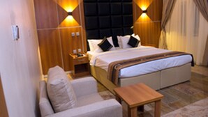 A hotel room with a bed, a sofa, a nightstand, and two wall-mounted lamps. - Room-presken Hotels Abuja-guest Room (Abuja)