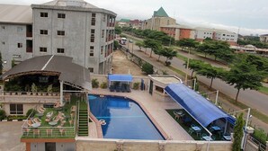 A swimming pool with a sunshade, outdoor seating, and a view of surrounding buildings. - Room-presken Hotels Abuja-guest Room (Abuja)