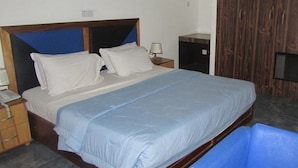 Una habitación de hotel estándar con una cama, mesitas de noche, una lámpara, un televisor y un armario.
