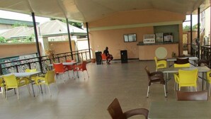 Un área de comedor interior con mesas, sillas y una barra, con una persona al fondo.