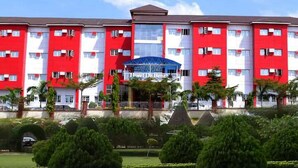A multi-story hotel with red and white exterior walls, a central entrance, and a well-maintained garden. - Room-hotel De Bently - Guest Room (Abuja)