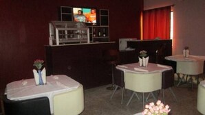 A hotel room with a television, a bar area, and multiple tables with chairs. - Room-joy House Hotel - Guest Room (Abuja)