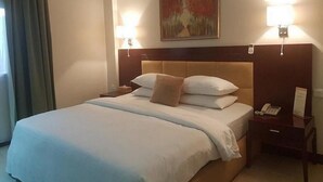 A hotel room with a large bed, two bedside lamps, a painting above the bed, and a telephone on the nightstand. - Room-joy House Hotel - Guest Room (Abuja)