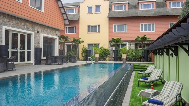 A swimming pool with lounge chairs, a stone wall, and a multi-story building with balconies. - Room-leola Hotel, Lagos-guest Room (Lagos)