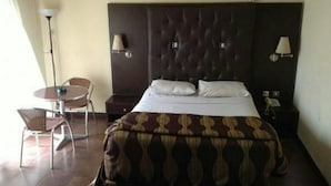 A hotel room with a bed, two bedside lamps, a chair, a small table, and a telephone. - Room-nelrose Hotel - Class King (Asaba)