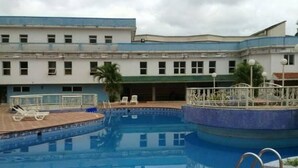 A swimming pool with a tiled deck, lounge chairs, and a building with multiple windows in the background. - Room-nelrose Hotel - Class King (Asaba)