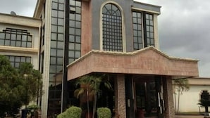 A multi-story building with large windows, a covered entrance, and a landscaped area with shrubs. - Room-nelrose Hotel - Class King (Asaba)