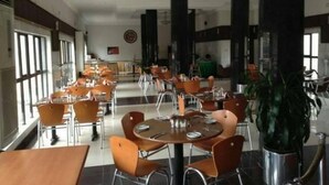 A spacious dining area with multiple tables and chairs, large windows, and a central plant. - Room-nelrose Hotel - Class King (Asaba)