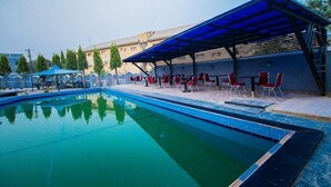 Une piscine dotée d’un espace détente abrité et de chaises rouges.