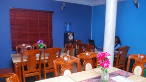 Un comedor con sillas y mesas de madera, un dispensador de agua, y una persona al fondo.