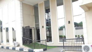 Um edifício com uma entrada ampla e aberta, uma escadaria que sobe e um portão de metal.