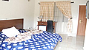Um quarto com uma cama, uma escrivaninha, uma cadeira, uma televisão e uma porta.