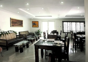 A spacious hotel dining area with a central table, surrounded by chairs, and a sofa. There are paintings on the walls and a large window providing natural light. - Room-prince Of Anthony 1960 Hotel (Lagos)