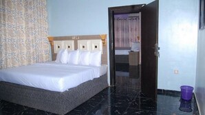 A hotel room with a bed, a door, a bathroom, and a patterned curtain. - Room-royal Park Hotel & Suite - Guest Ro (Asaba)