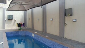 A swimming pool with a tiled edge, a covered seating area, and a television mounted on the wall. - Room-royal Park Hotel & Suite - Guest Ro (Asaba)