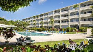 Un hôtel doté d’une piscine, de chaises longues et d’un grand bâtiment comportant de nombreux balcons.