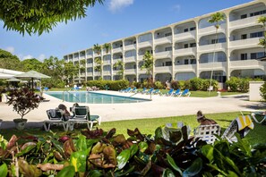 A hotel with a pool, lounge chairs, and a multi-story building with balconies. - Golden View #115 - by Zenbreak (Holetown)