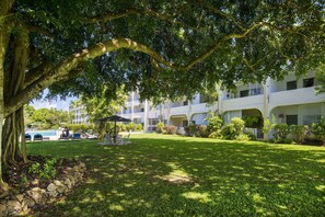 Un exuberante jardín con un pabellón, una piscina y un edificio con varios balcones.