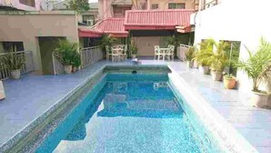 Una piscina rectangular con bordeado de azulejos, rodeada de plantas en macetas y mobiliario de exterior.